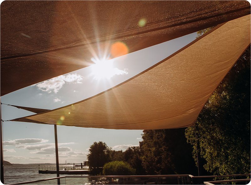 A sunny view of a lake seen from underneath triangular sun shade sails.